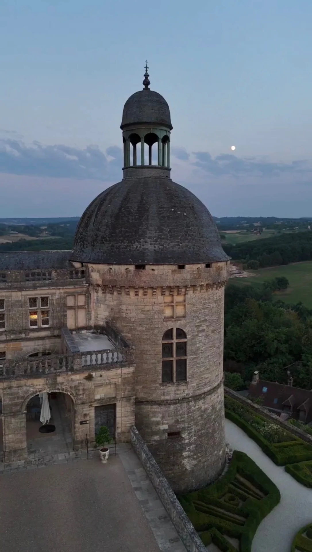Tour en pierre du château de Hautefort sous la lune, avec le paysage du Périgord à l’arrière-plan