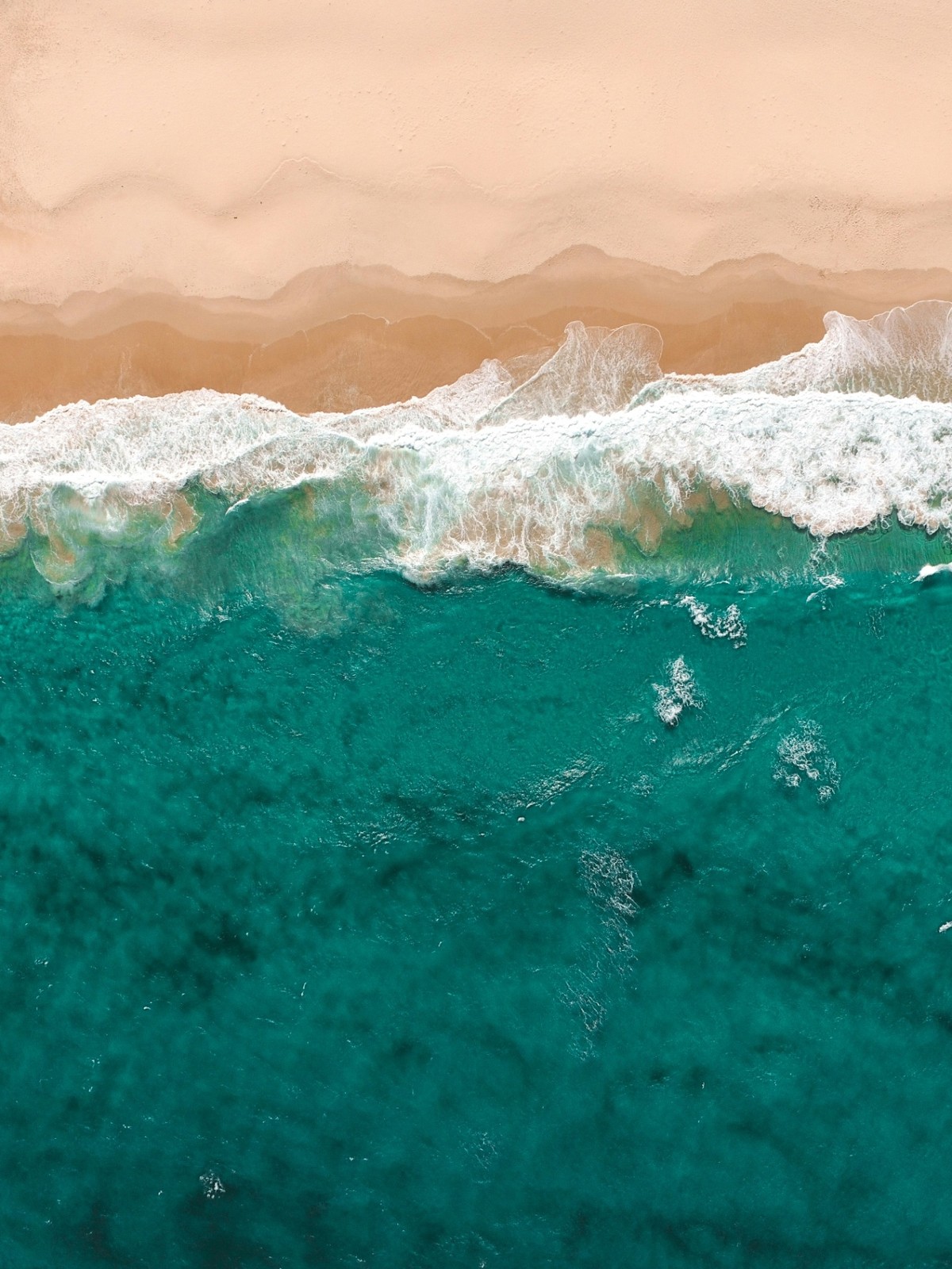 Vue aérienne d'une plage landaise : sable doré, écume blanche d'une vague qui se déroule et eau turquoise de l'océan Atlantique